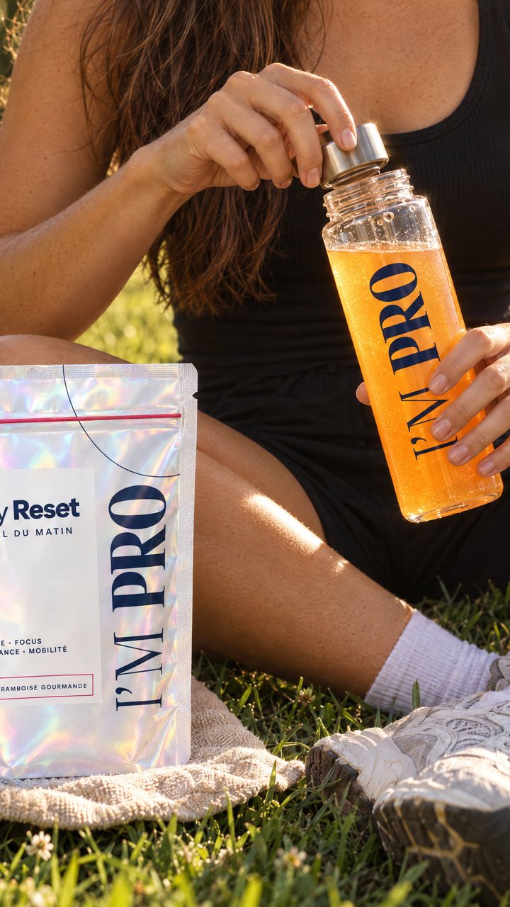 Une femme assise dans l’herbe ouvre une gourde orange, à côté du sachet Day Reset